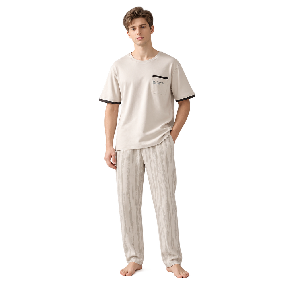 A man modeling a two-piece pajama set consisting of a short-sleeve crewneck t-shirt in cream with black trim on the sleeve cuffs and chest pocket, paired with matching cream pajama pants with a subtle vertical stripe pattern.