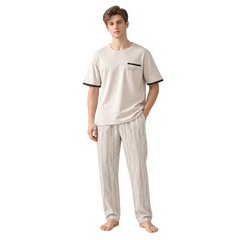 A man modeling a two-piece pajama set consisting of a short-sleeve crewneck t-shirt in cream with black trim on the sleeve cuffs and chest pocket, paired with matching cream pajama pants with a subtle vertical stripe pattern.