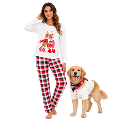 A woman wearing a white long-sleeve pajama top with a Christmas reindeer graphic and red/black plaid pajama pants stands next to a golden retriever dog wearing a matching white shirt and red/black plaid neck gaiter, on a solid white background.